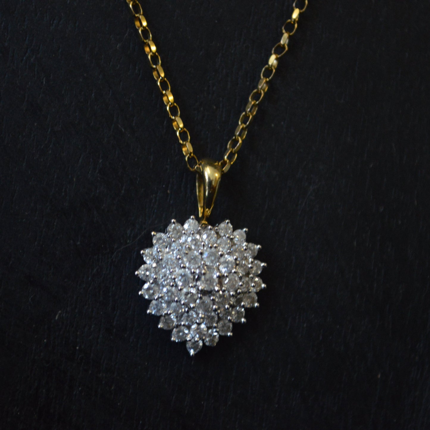 A vintage 18ct gold diamond heart pendant on a 9ct gold box chain against a black background.