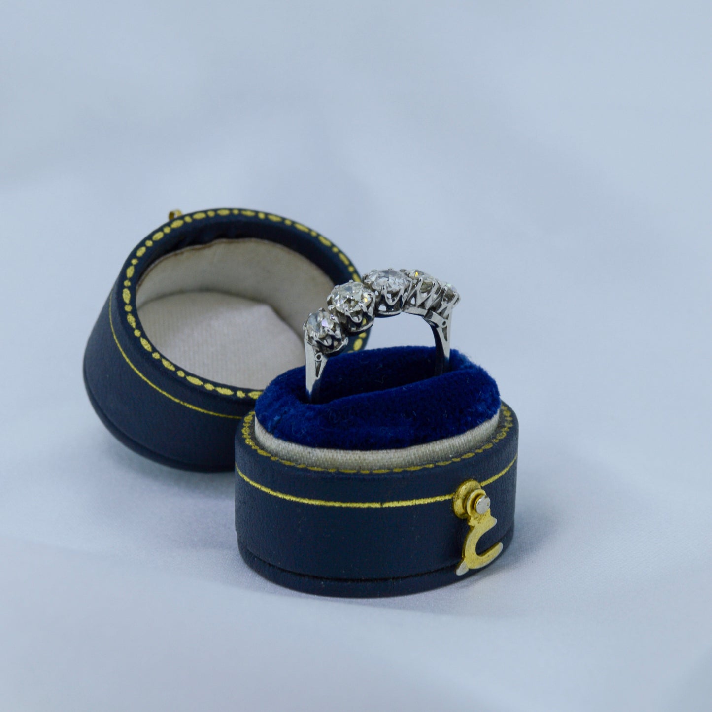  ring with blue cushion in a black jewelry box on a light gray background